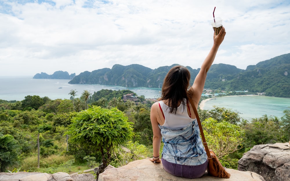 a woman sitting on top of a rock with her arms in the air