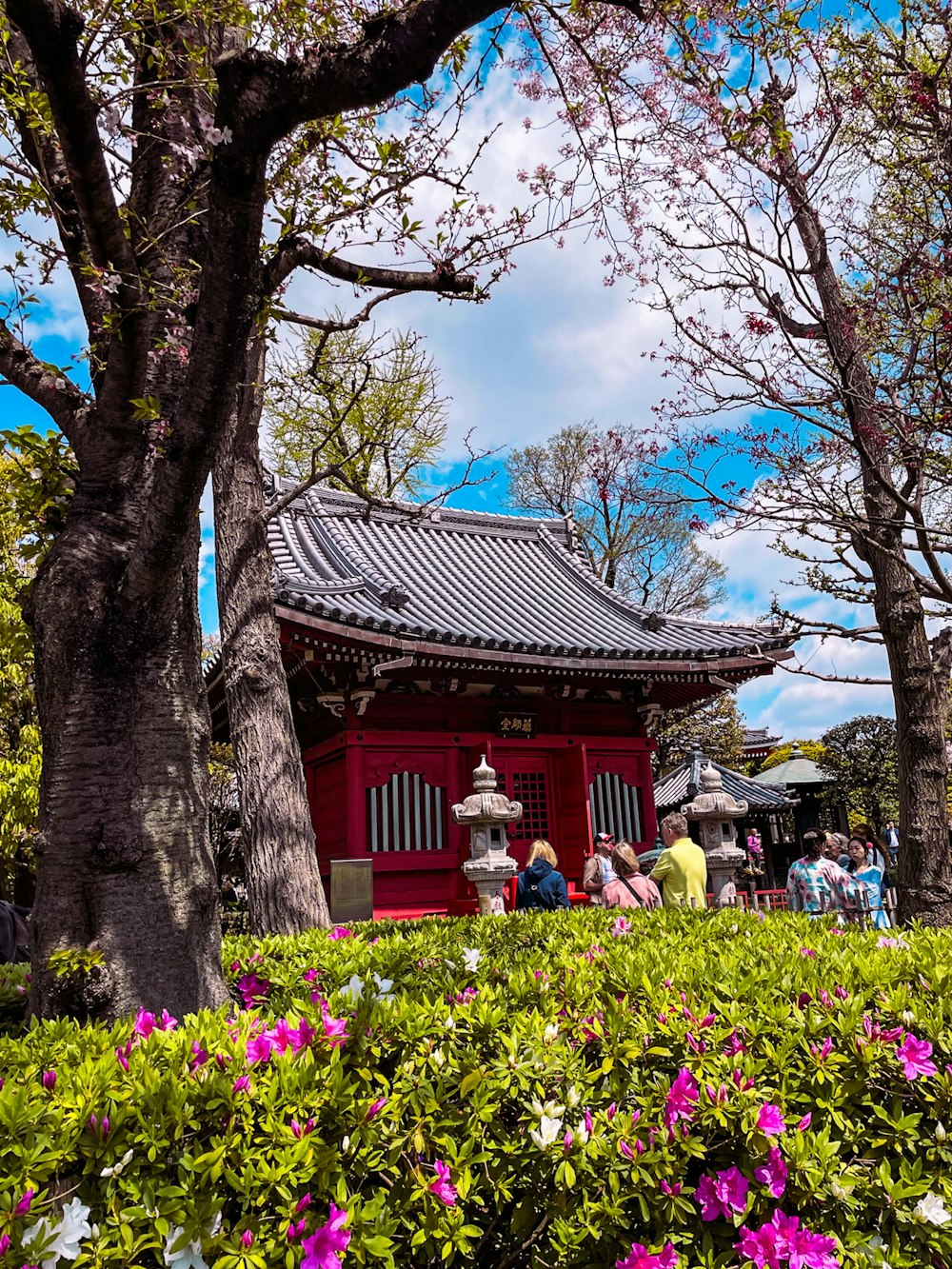 a small red building surrounded by trees and flowers