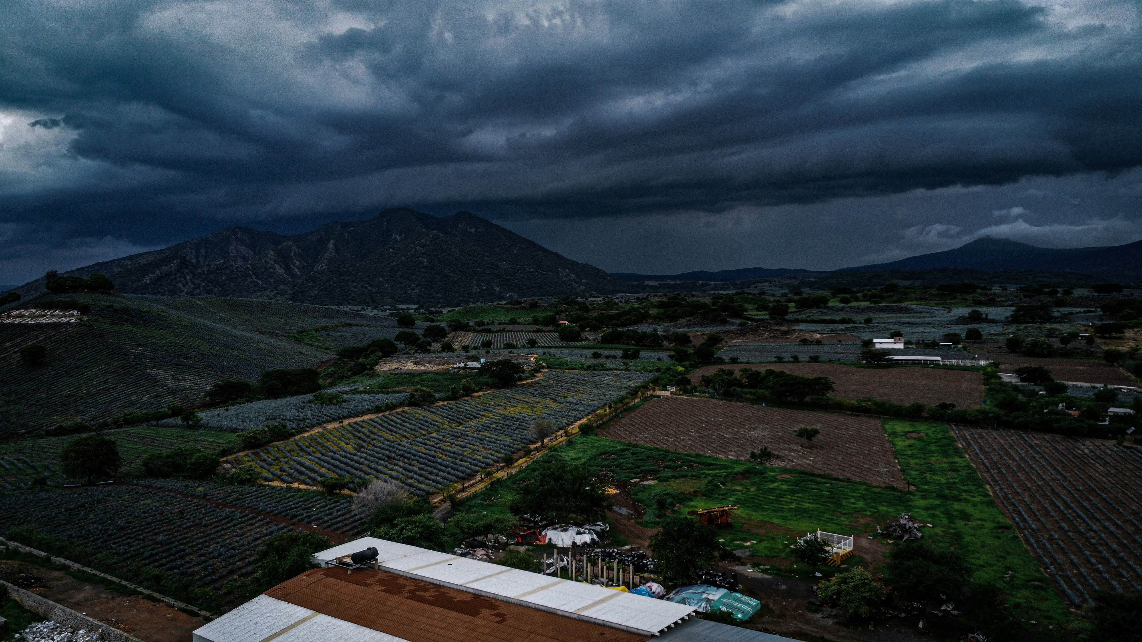 a storm rolls in over a farm with mountains in the background