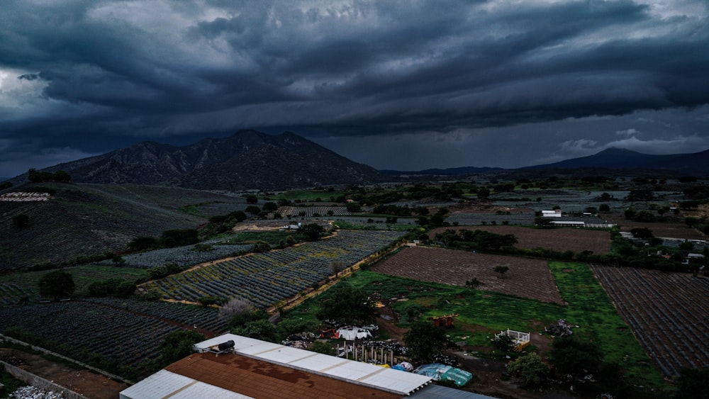 a storm rolls in over a farm with mountains in the background