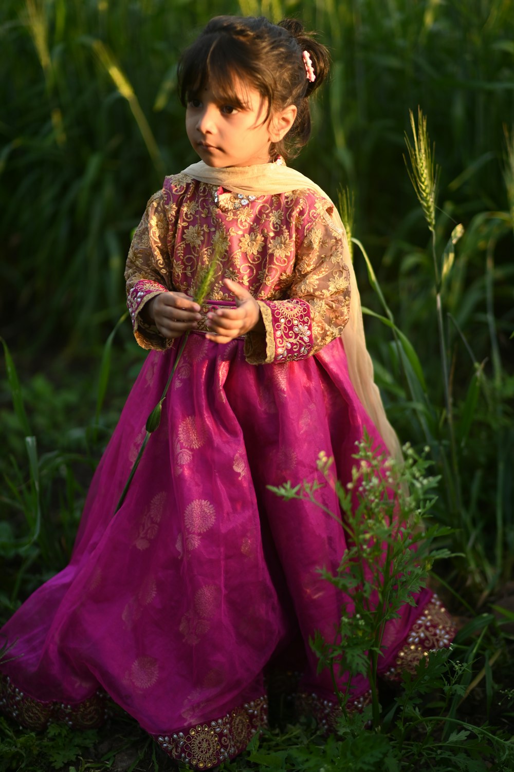 a little girl in a pink dress standing in a field