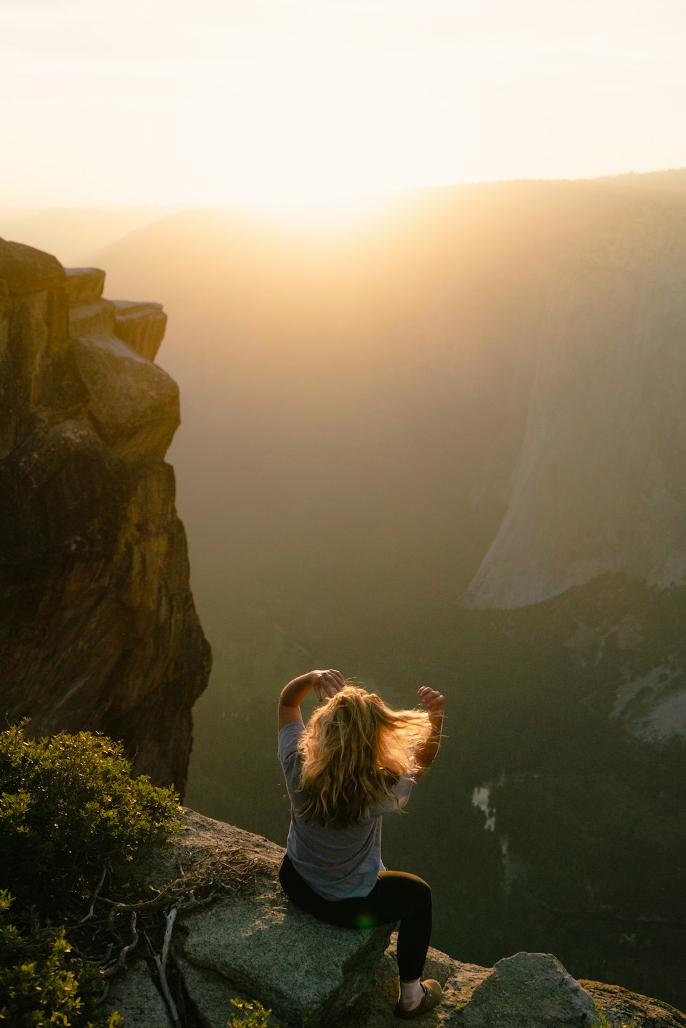 una mujer sentada en la cima de un acantilado con vistas a un valle