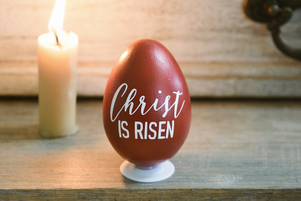 a red egg sitting on top of a table next to a candle