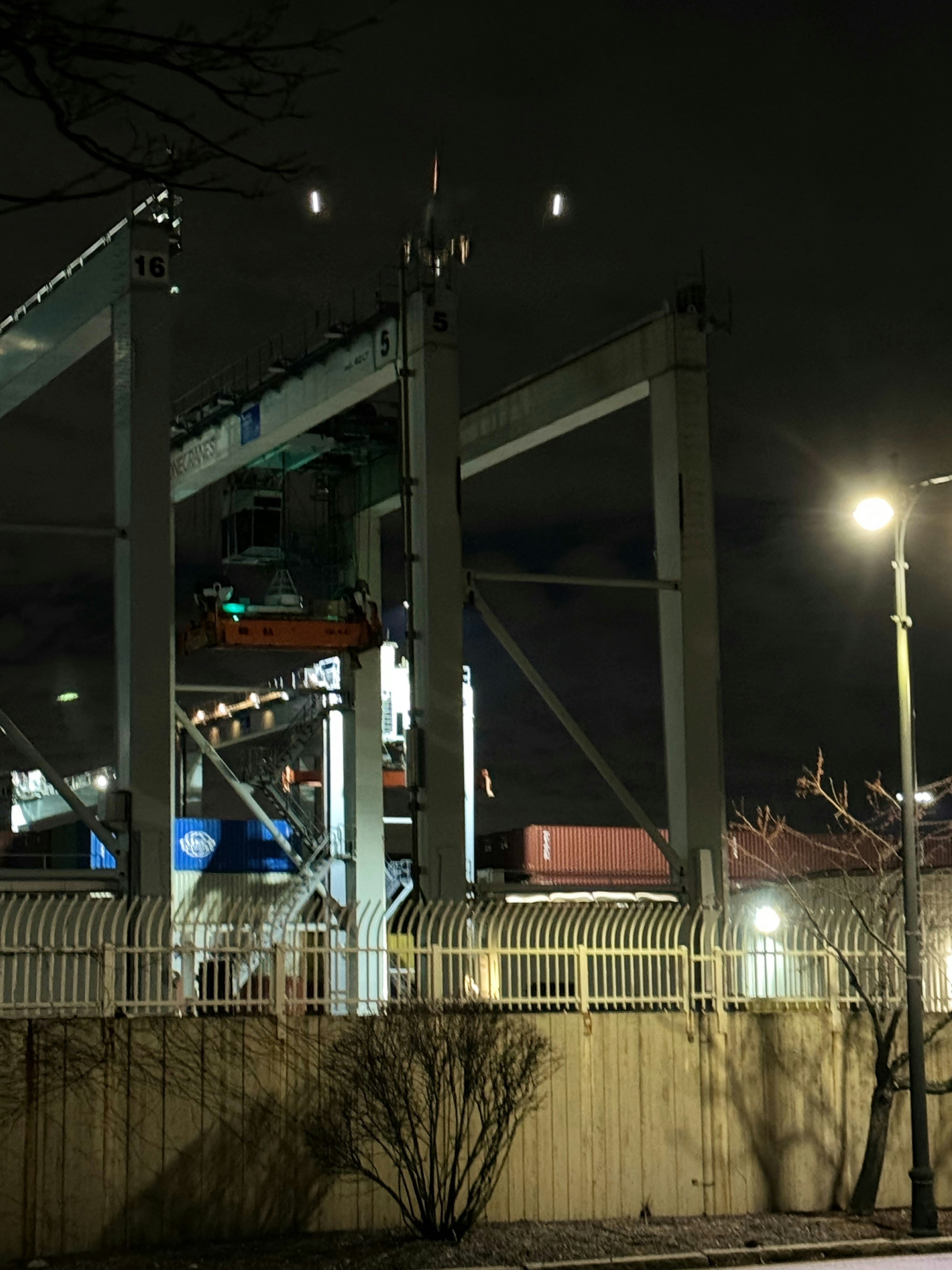 Port crane lifting shipping container at night, bright spotlights, industrial waterfront