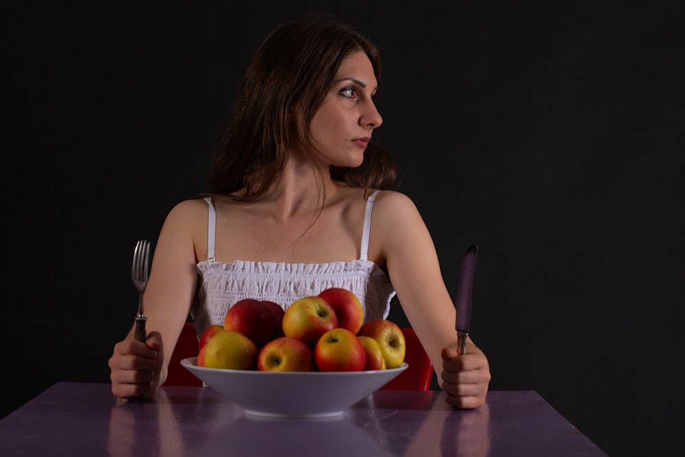 a woman sitting at a table with a bowl of apples