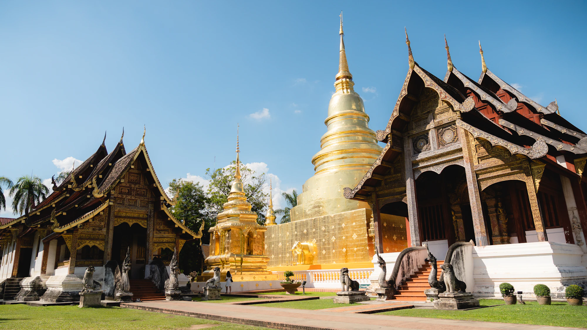 A gilded chedi rising behind the tiered, gold-trimmed roofs of a Lanna temple in Chiang Mai under a clear blue sky