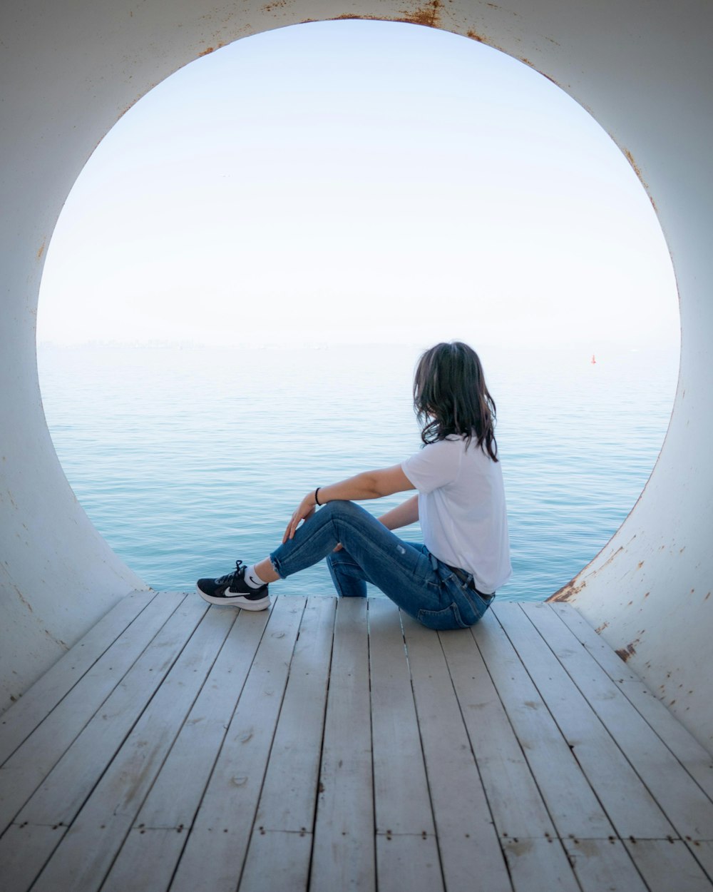 a person sitting on a wooden floor looking out at the water