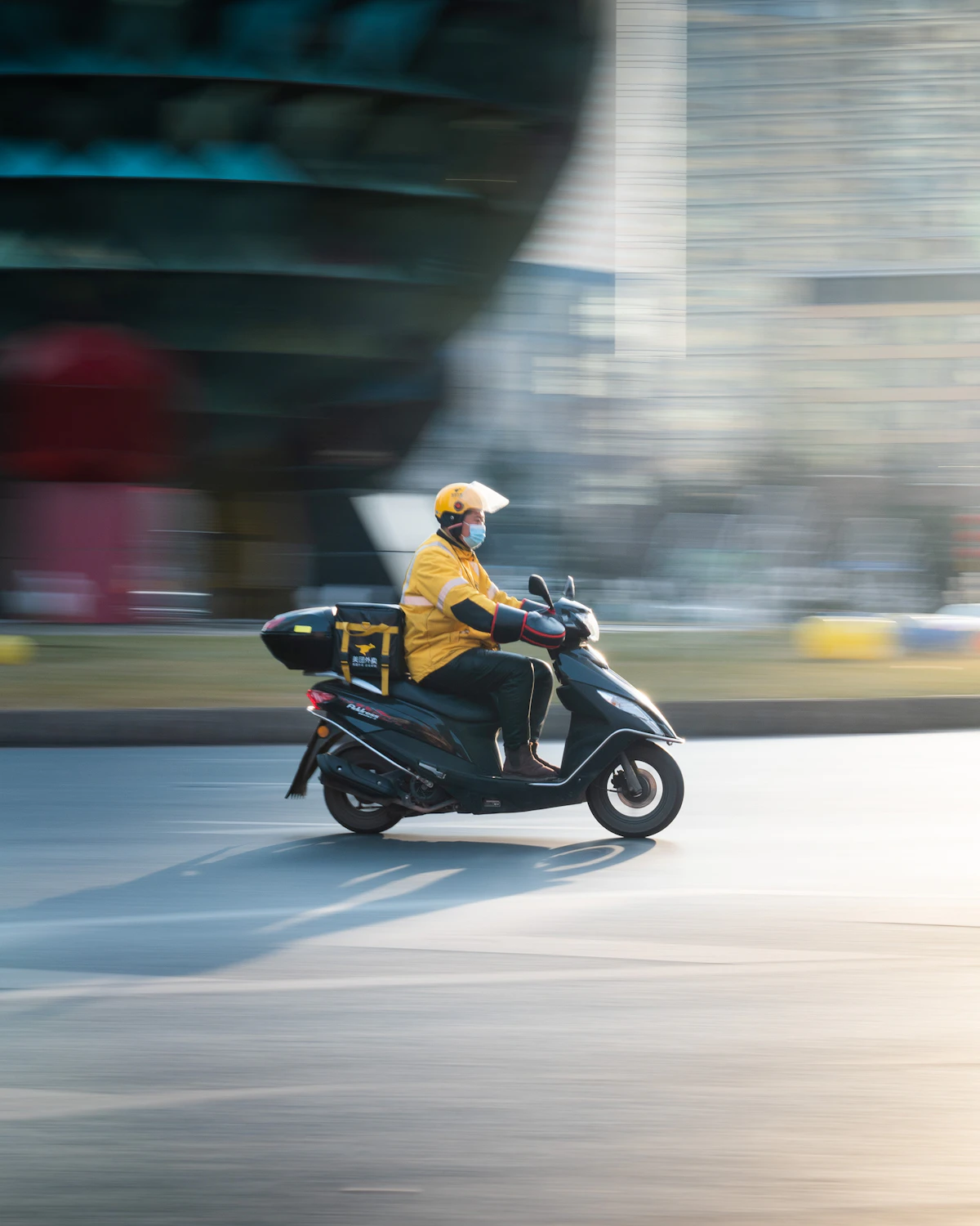 A delivery rider in a yellow jacket riding a scooter