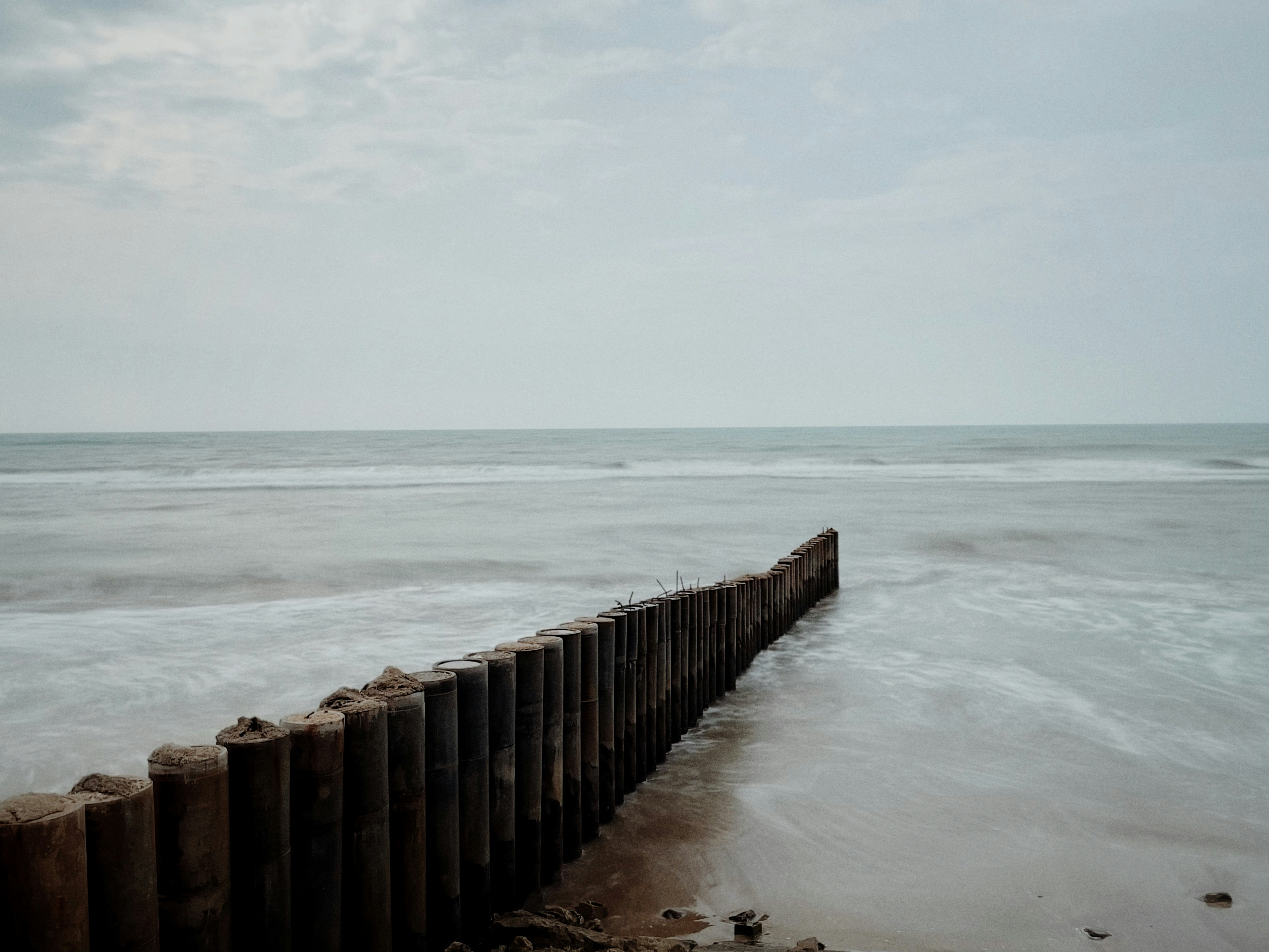 A long wooden fence sitting on top of a beach next to the ocean