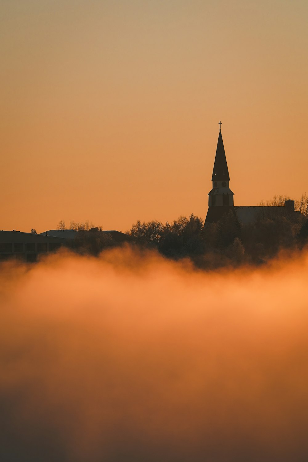 a church steeple rises above the clouds at sunset
