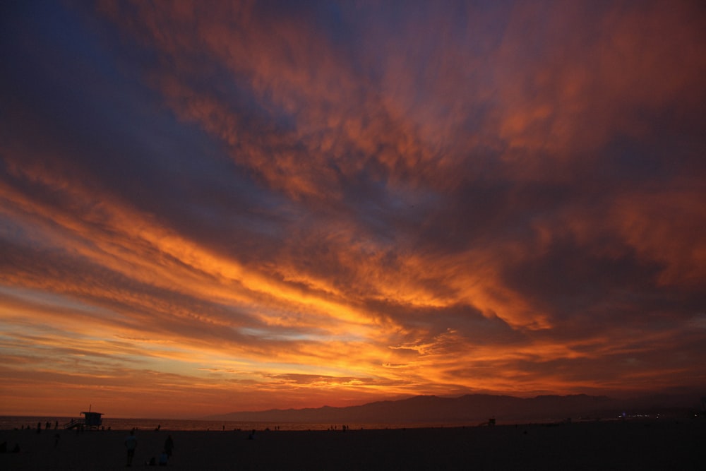 a beautiful sunset over a beach with people walking on the sand