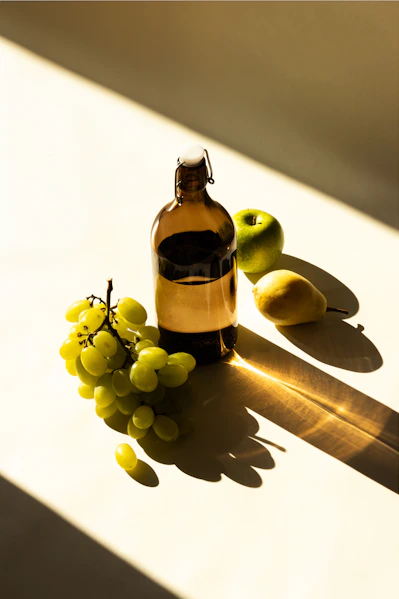 une bouteille de vinaigre de cidre à coté de raison, poire et pomme sur la table