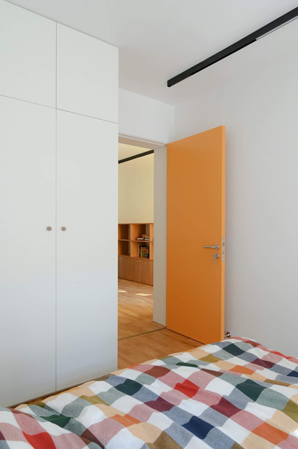 a bedroom with a bed, cupboards, and an orange door