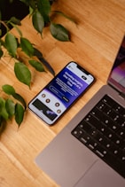 a cell phone sitting on top of a wooden table next to a laptop