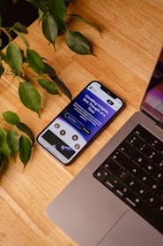a cell phone sitting on top of a wooden table next to a laptop