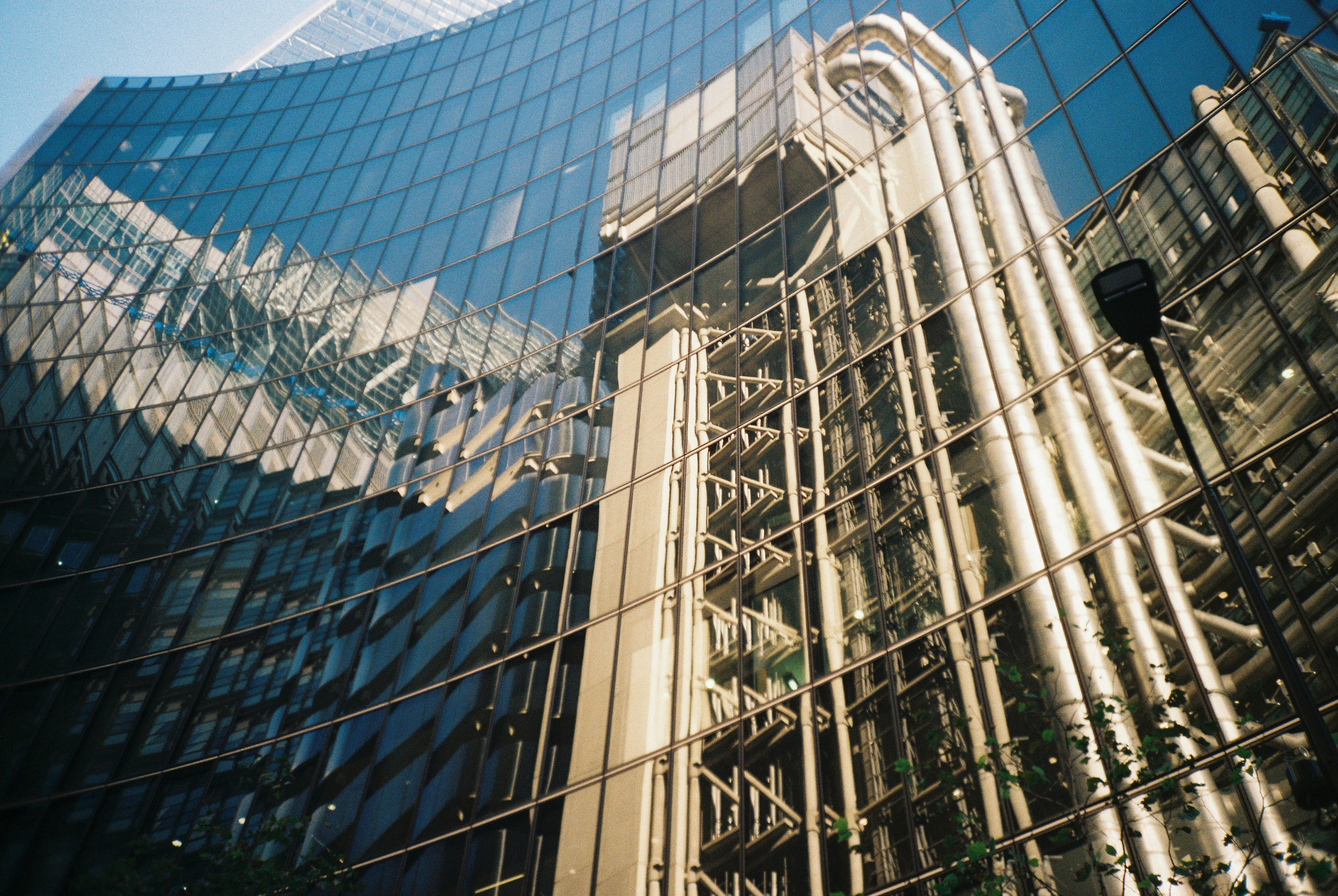 The futuristic architecture of the Lloyd’s building reflected in hundreds of windows of offices nearby on a bright, clear day in the City of London. Shot on film.