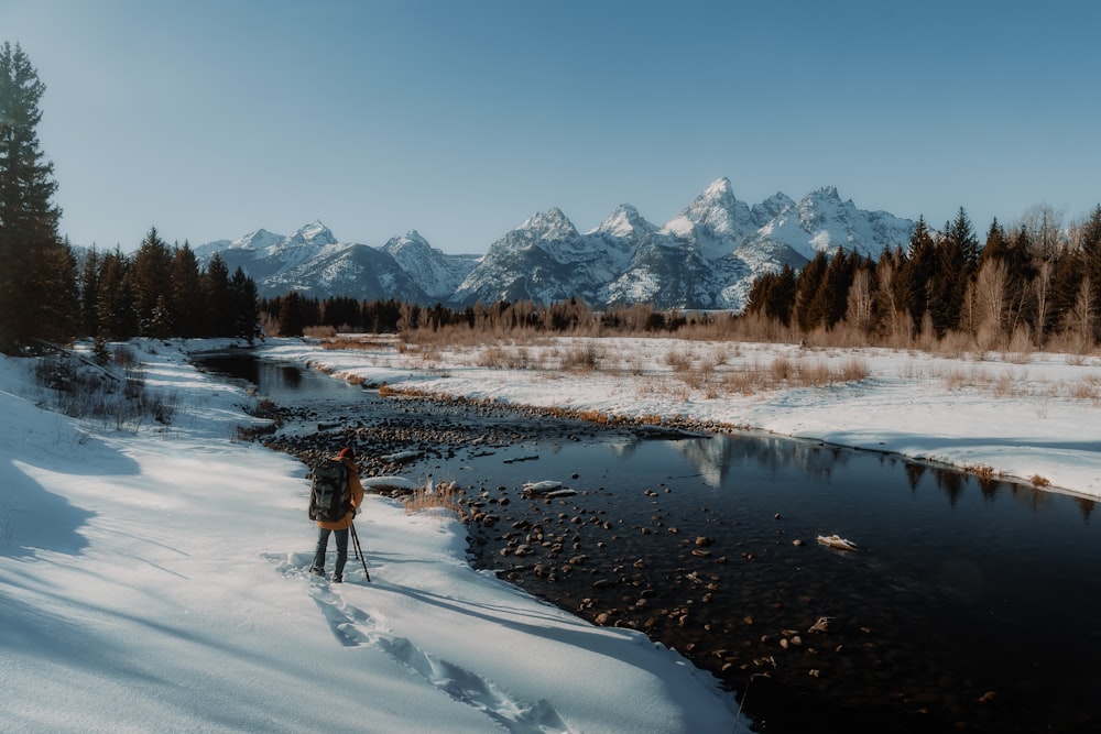 a person standing in the snow near a river