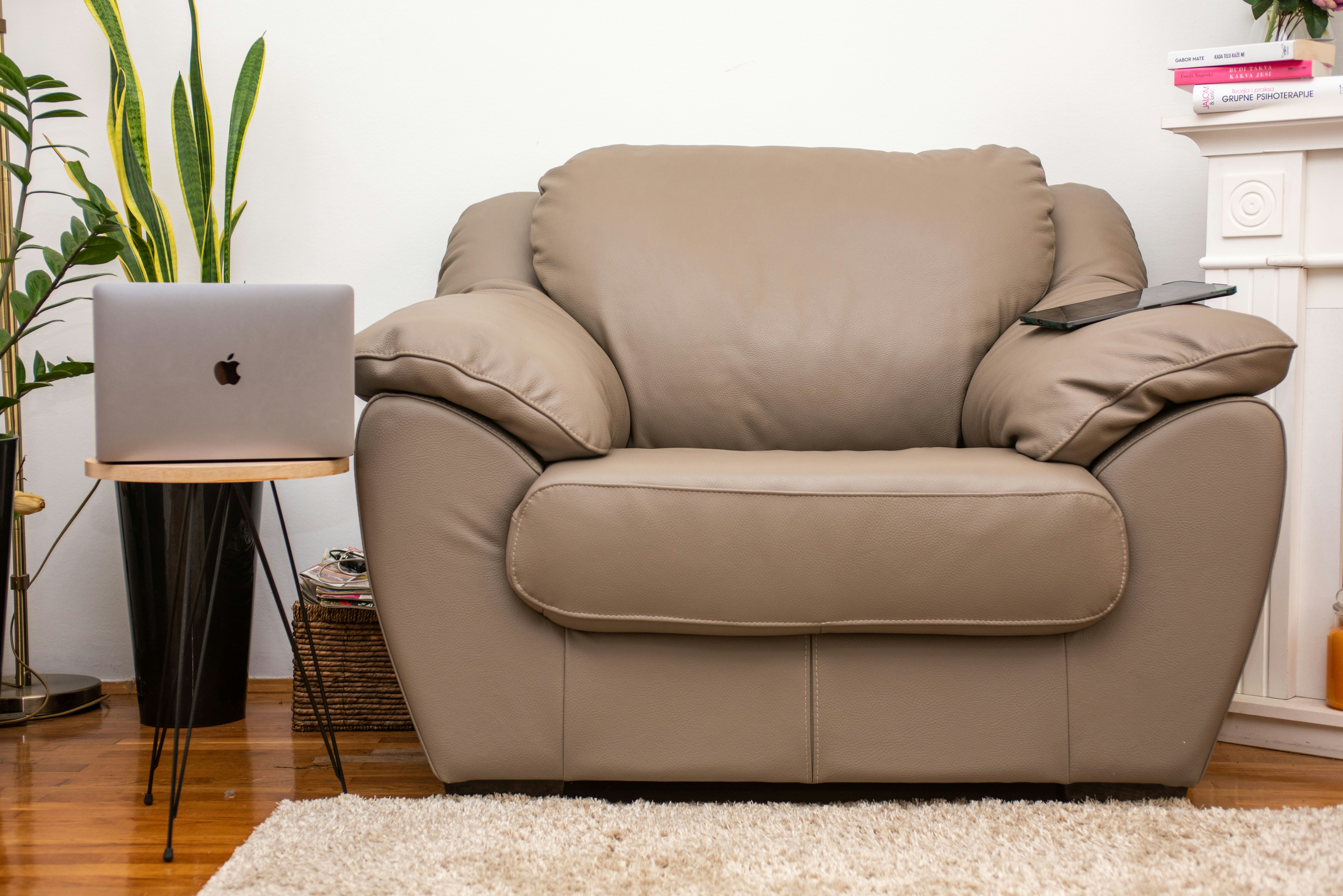 a brown leather chair sitting in a living room next to a laptop computer