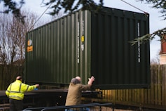 a couple of men standing next to a green container