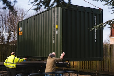 a couple of men standing next to a green container