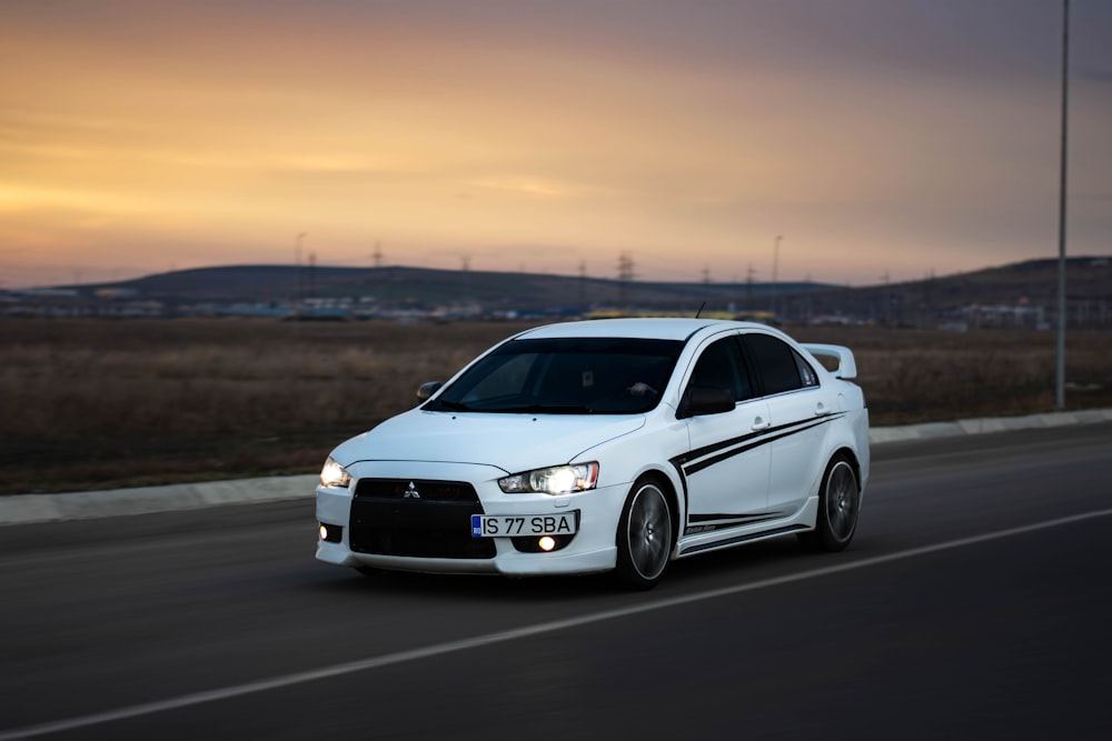 a white car driving down a road next to a field