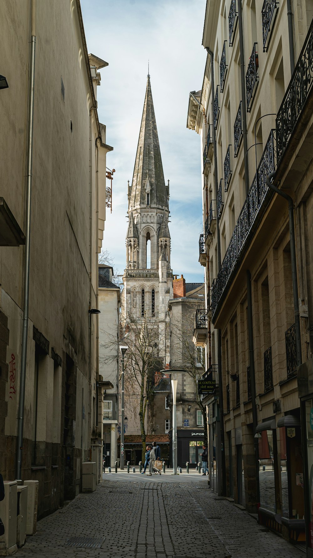 a narrow city street with a church steeple in the background