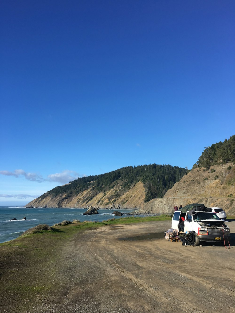 a van parked on the side of a dirt road next to the ocean