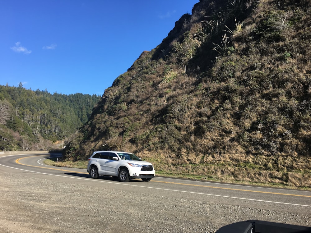 a white car driving down a curvy road next to a mountain