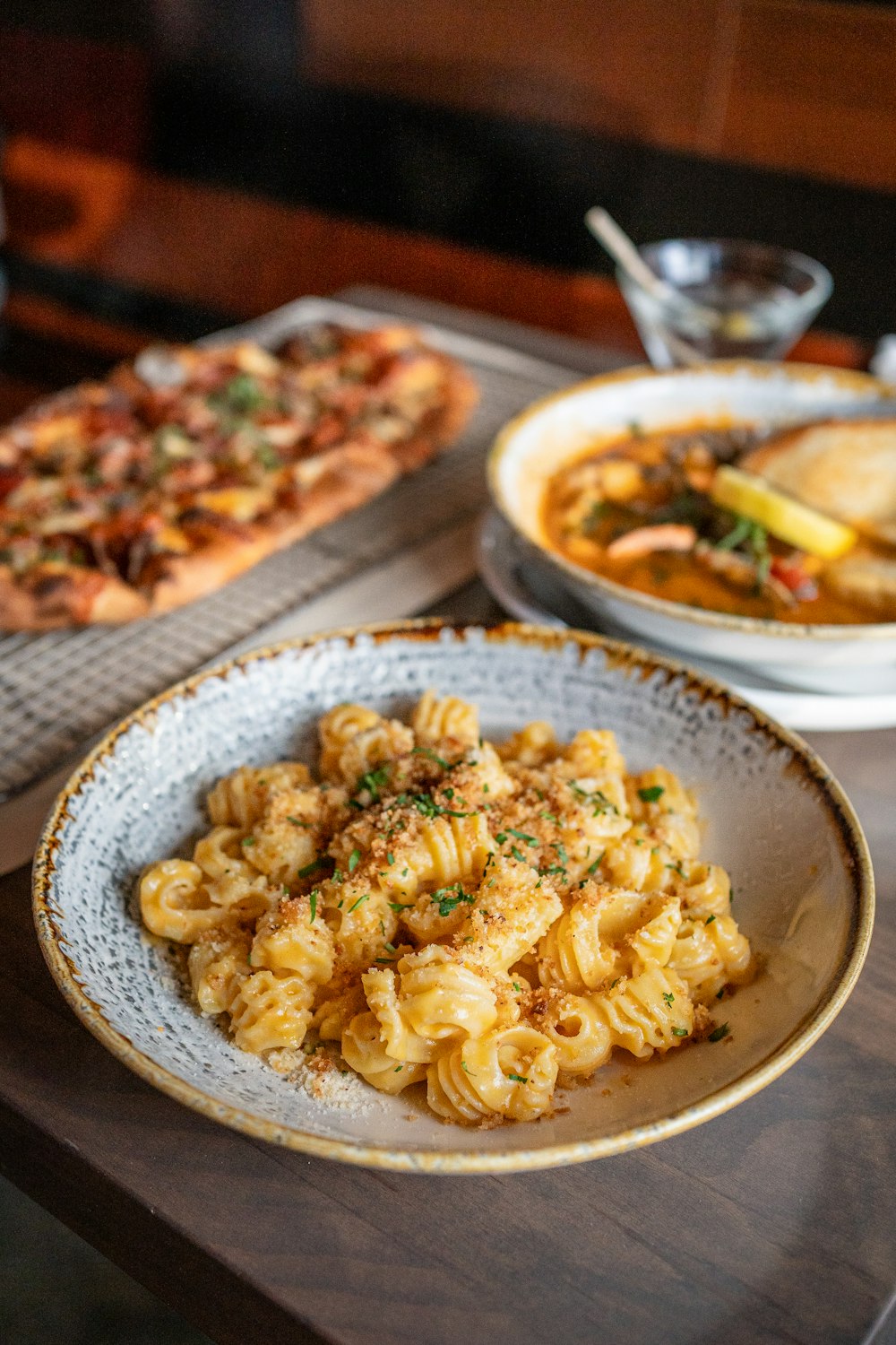 a bowl of pasta and a plate of pizza on a table