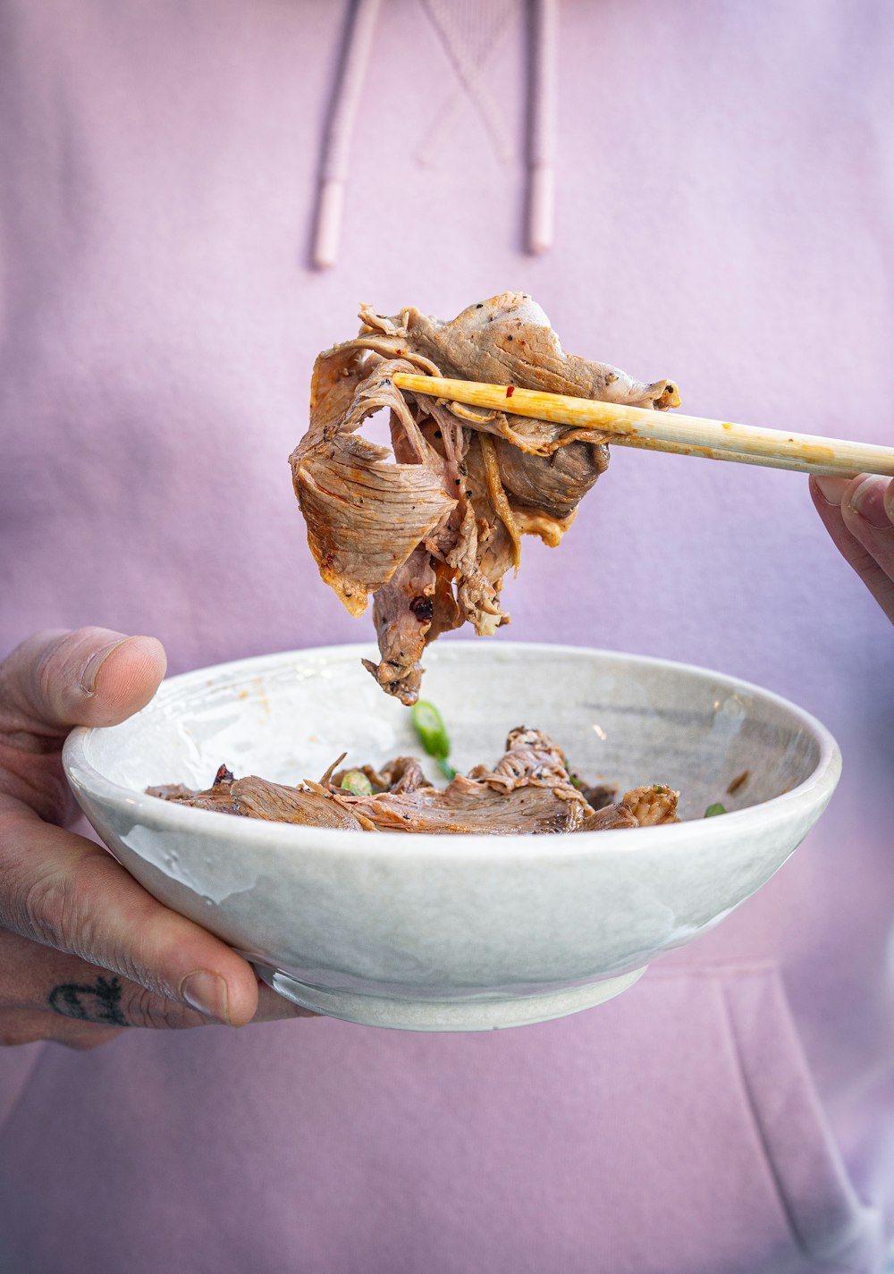 a person holding a bowl of food with chopsticks