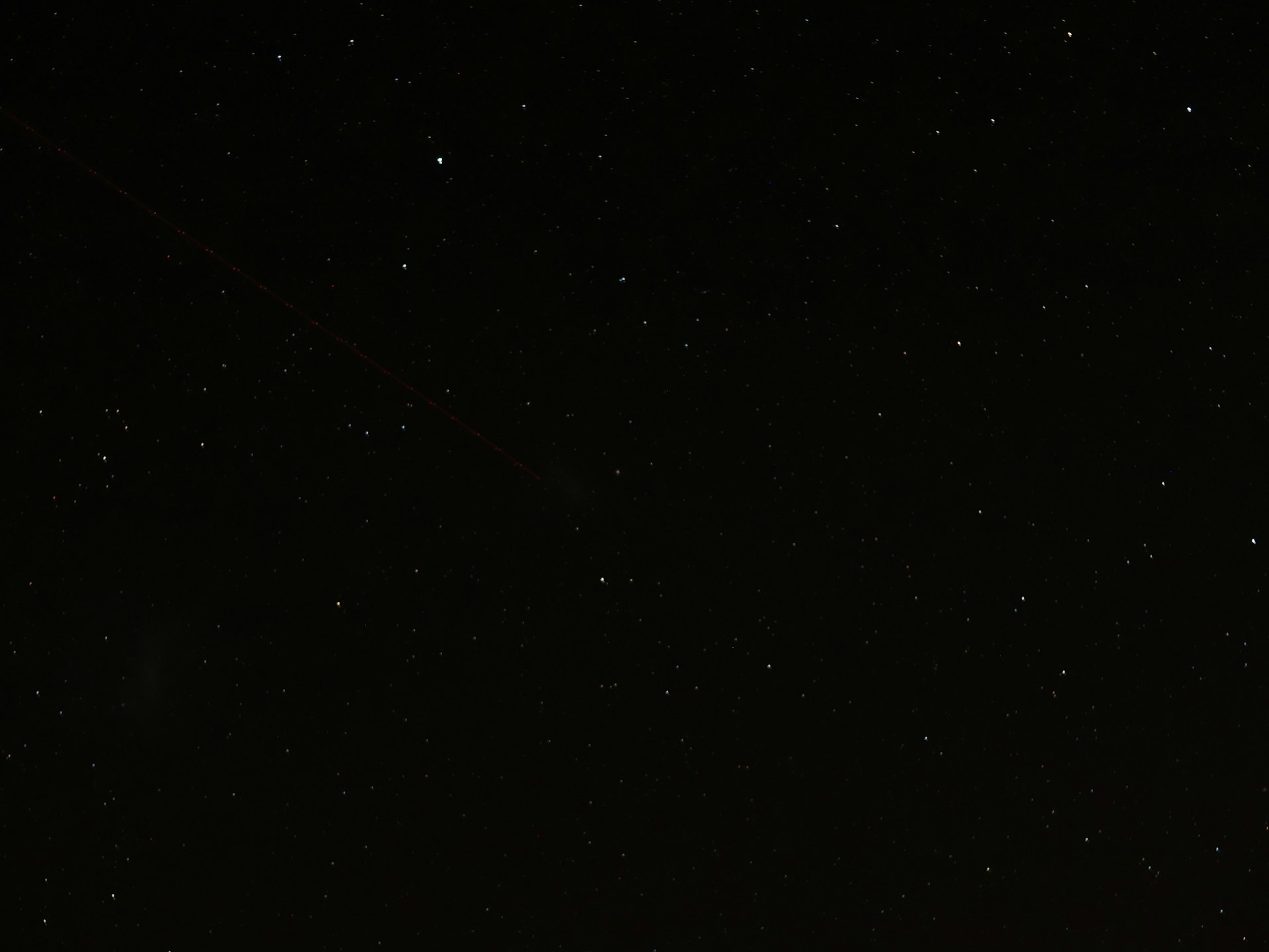 a dark sky with stars and a plane in the distance