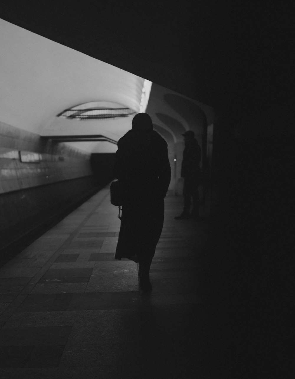 a black and white photo of a person walking in a subway
