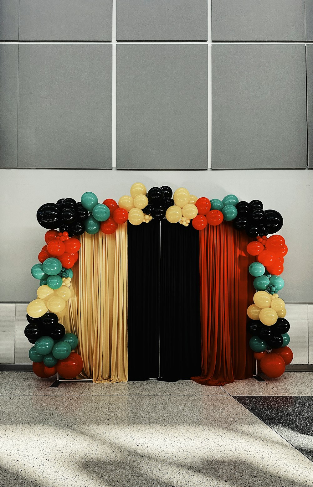 un arco de globos negros, naranjas y dorados con cortinas negras