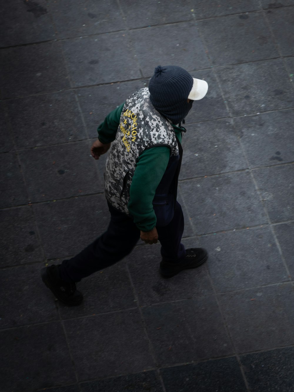 a man walking down a sidewalk with a hat on