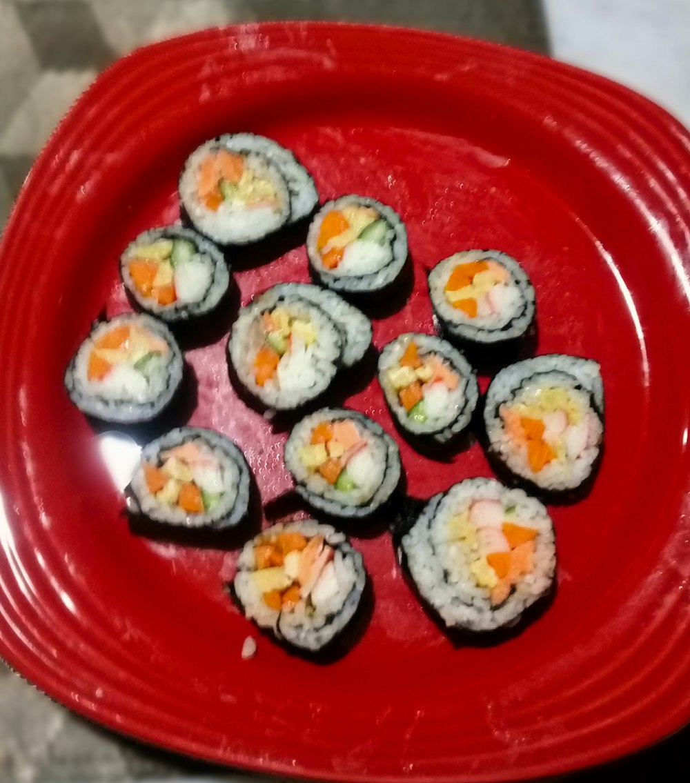 a red plate topped with sushi and vegetables