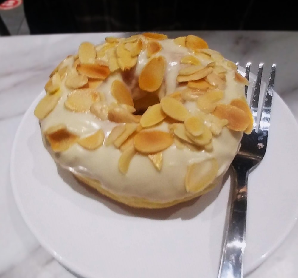 a white plate topped with a frosted donut covered in almonds