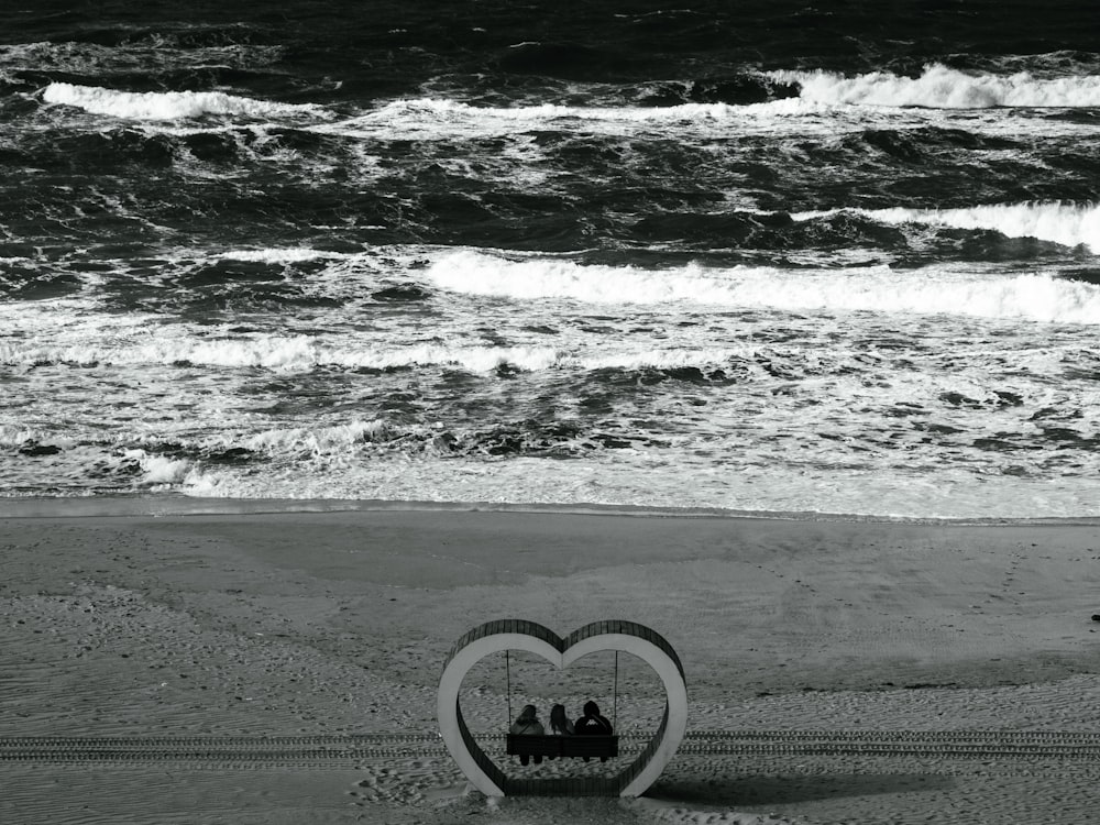 a heart shaped frame with two people riding on a swing on the beach