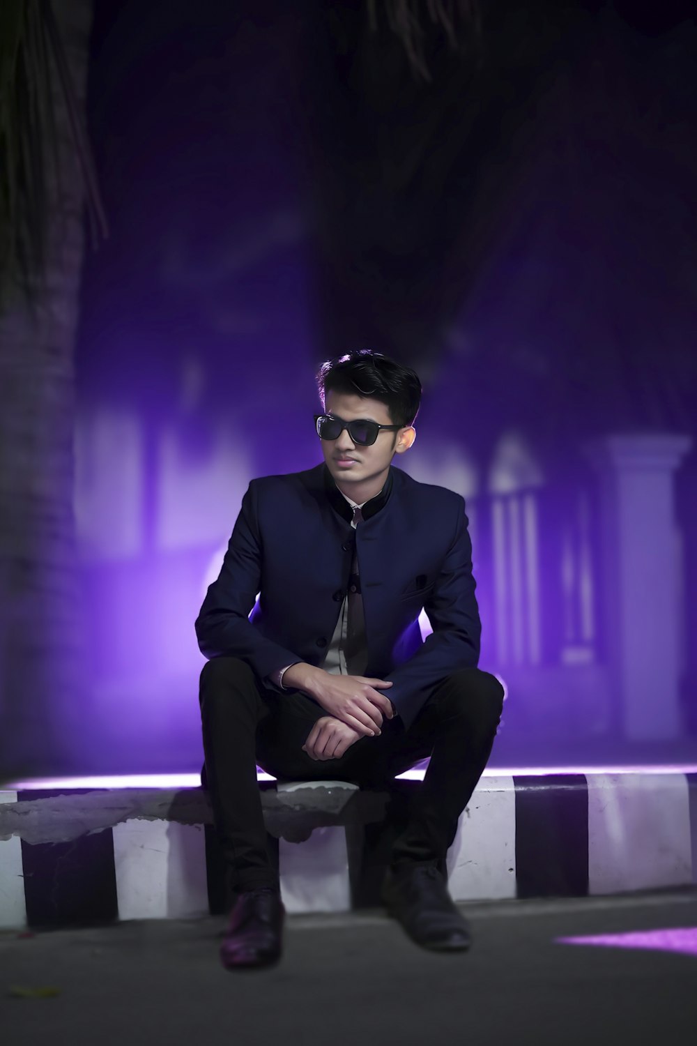 a man in a suit and sunglasses sitting on a bench