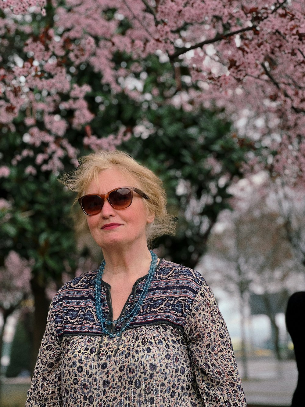 a woman in sunglasses standing under a tree with pink flowers