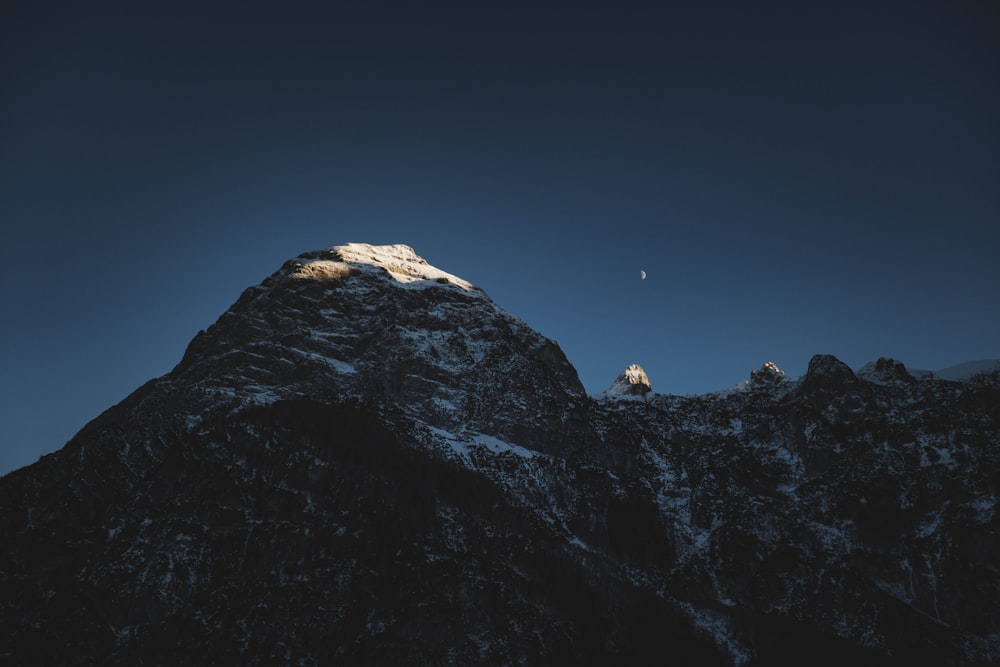 the top of a mountain with a moon in the sky
