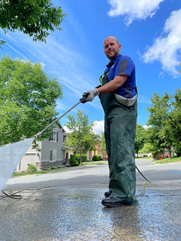 A technician washing a hard surface with a pressure washer.