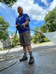 a man in a blue shirt is washing a driveway