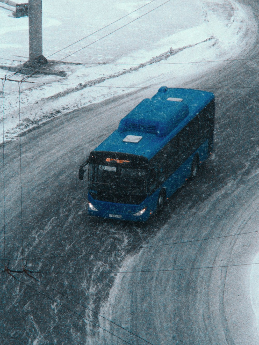 a blue bus driving down a snow covered road