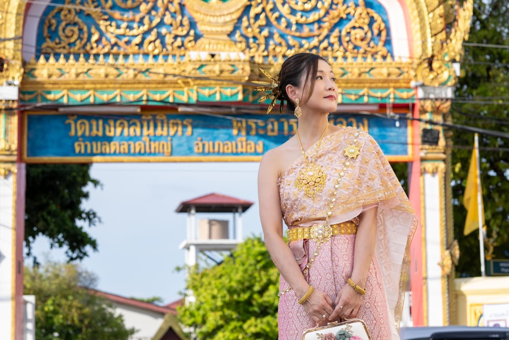 a woman in a pink and gold dress standing in front of a sign