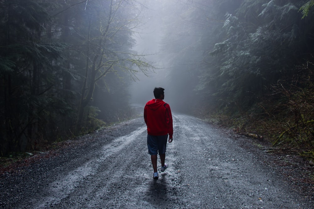um homem caminhando por uma estrada no meio de uma floresta