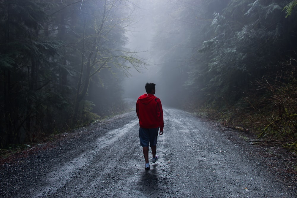 a man walking down a road in the middle of a forest