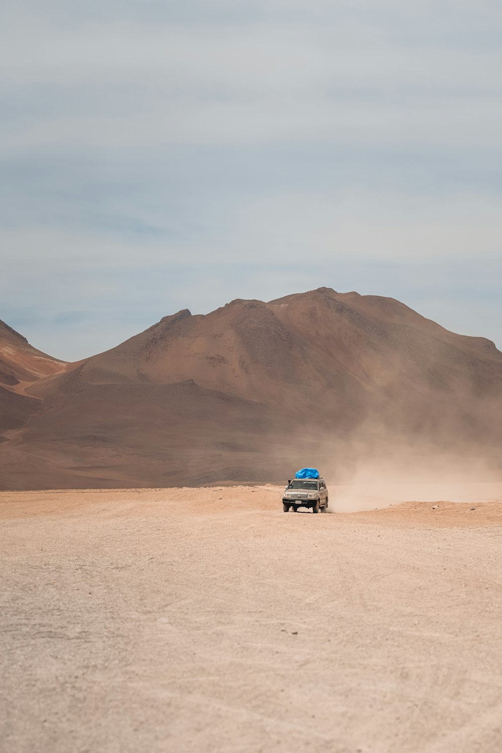 a truck driving through a desert with mountains in the background