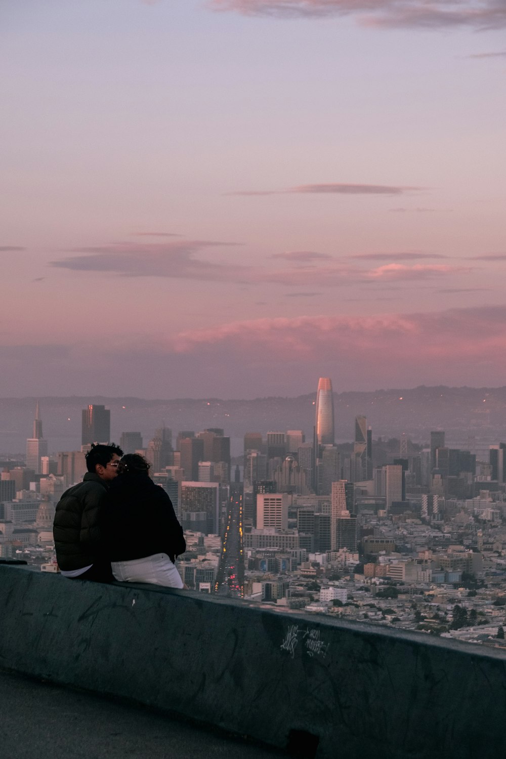 two people sitting on a ledge overlooking a city