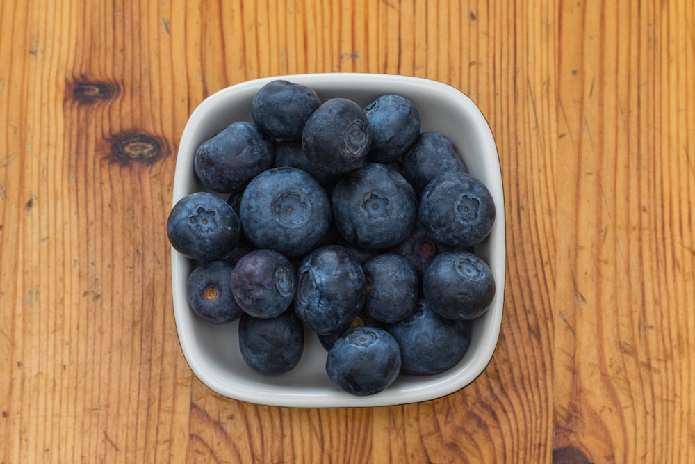a white bowl filled with blueberries on top of a wooden table