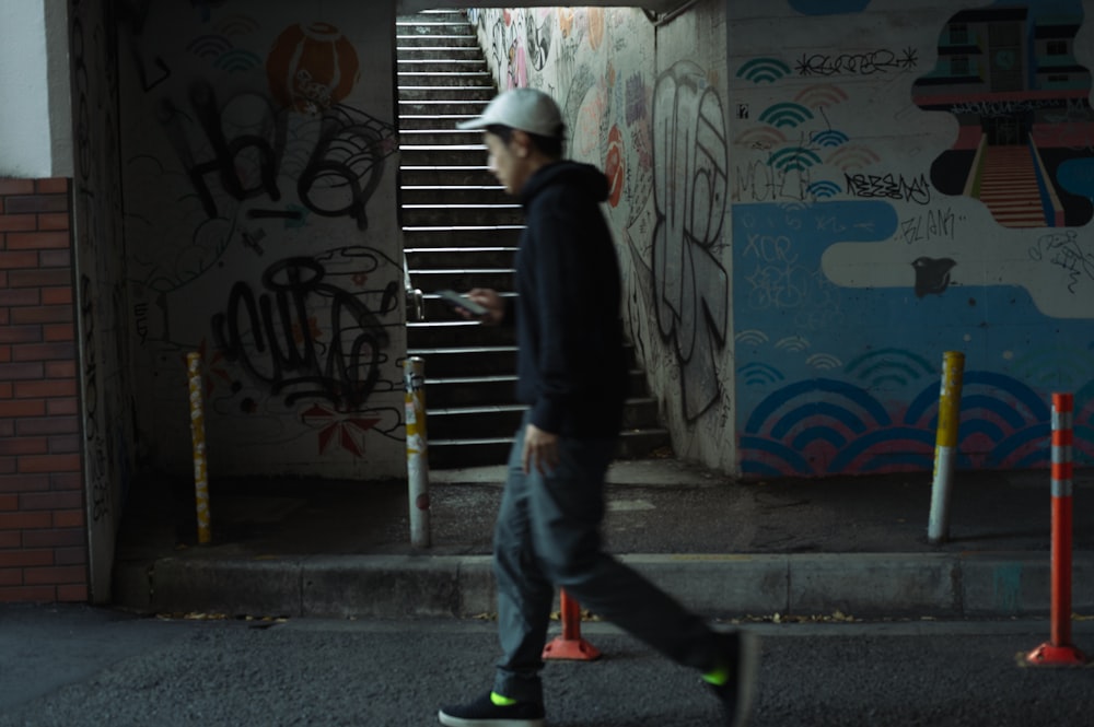 um homem caminhando por uma rua ao lado de um muro coberto de pichação